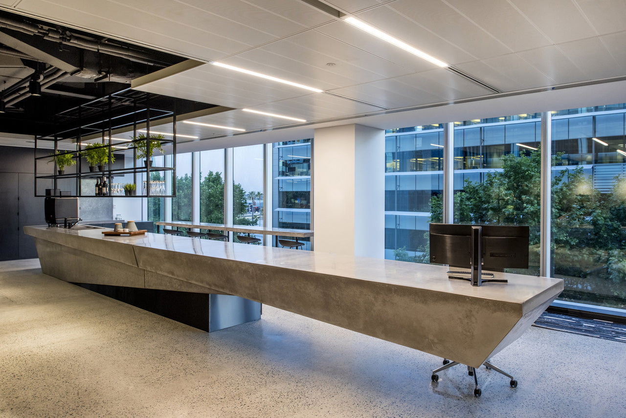 Modern office interior with a long cantilever concrete reception desk and large windows.