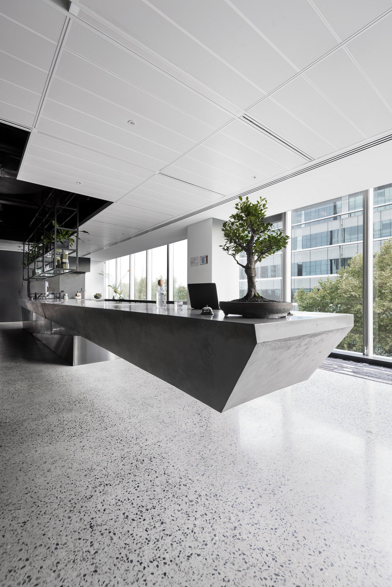 Modern office interior with a large concrete reception desk and large windows.
