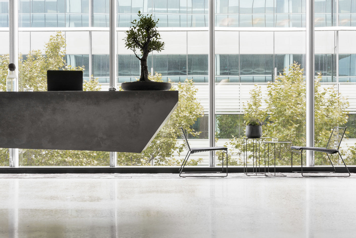 Modern office interior with a large concrete reception desk and chairs in front of large windows.