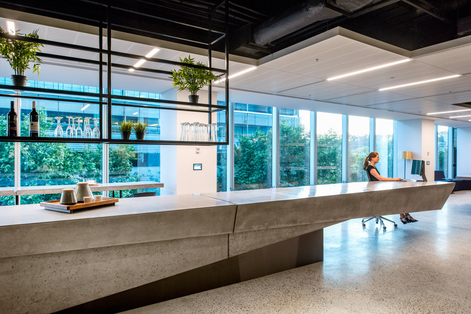 Modern office interior with a concrete reception desk and large windows.