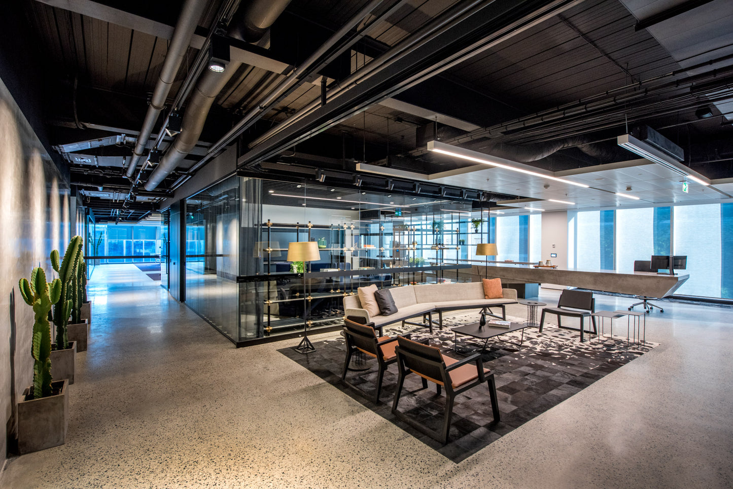 Modern office space with a lounge area featuring a sofa, chairs, a coffee table and a concrete reception desk.
