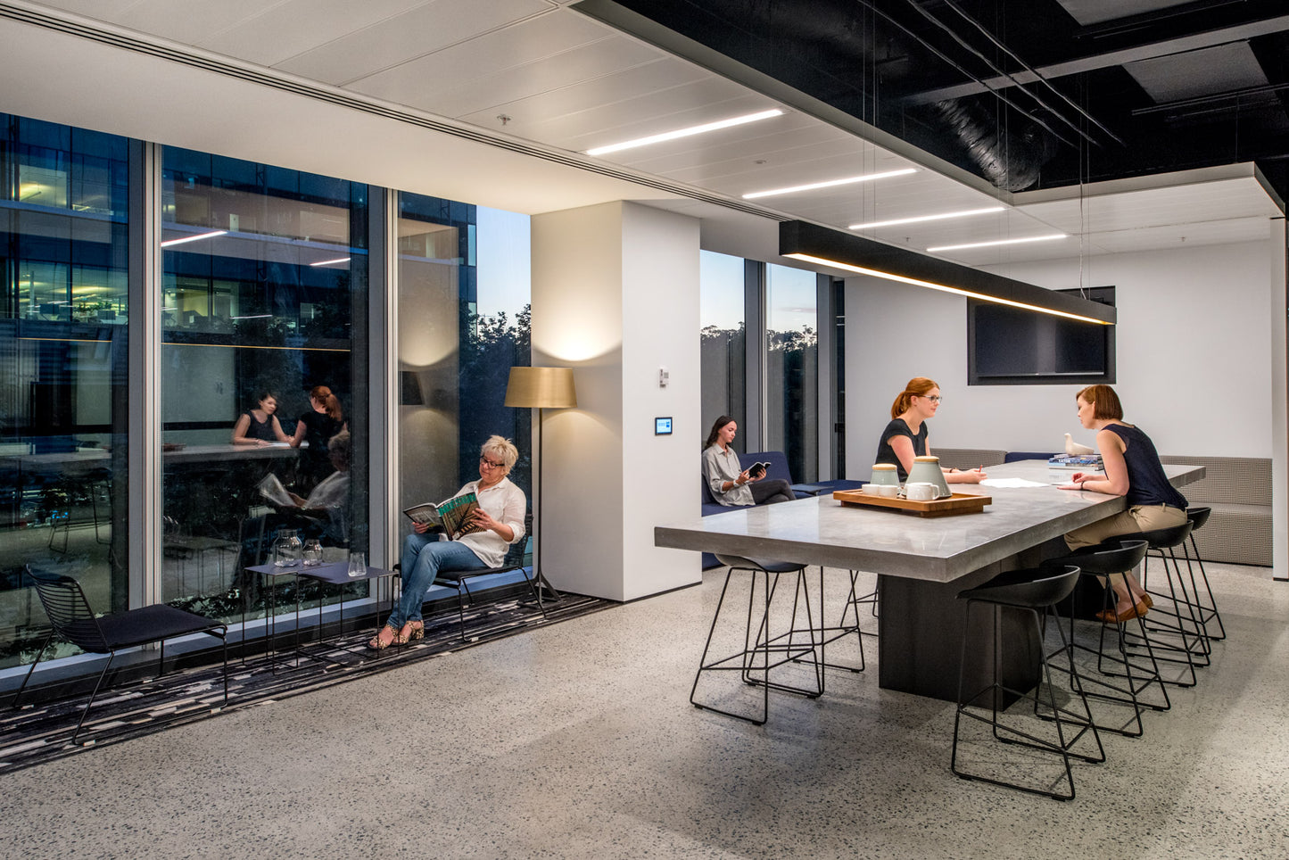 Modern office space with people working and interacting around a large concrete table.