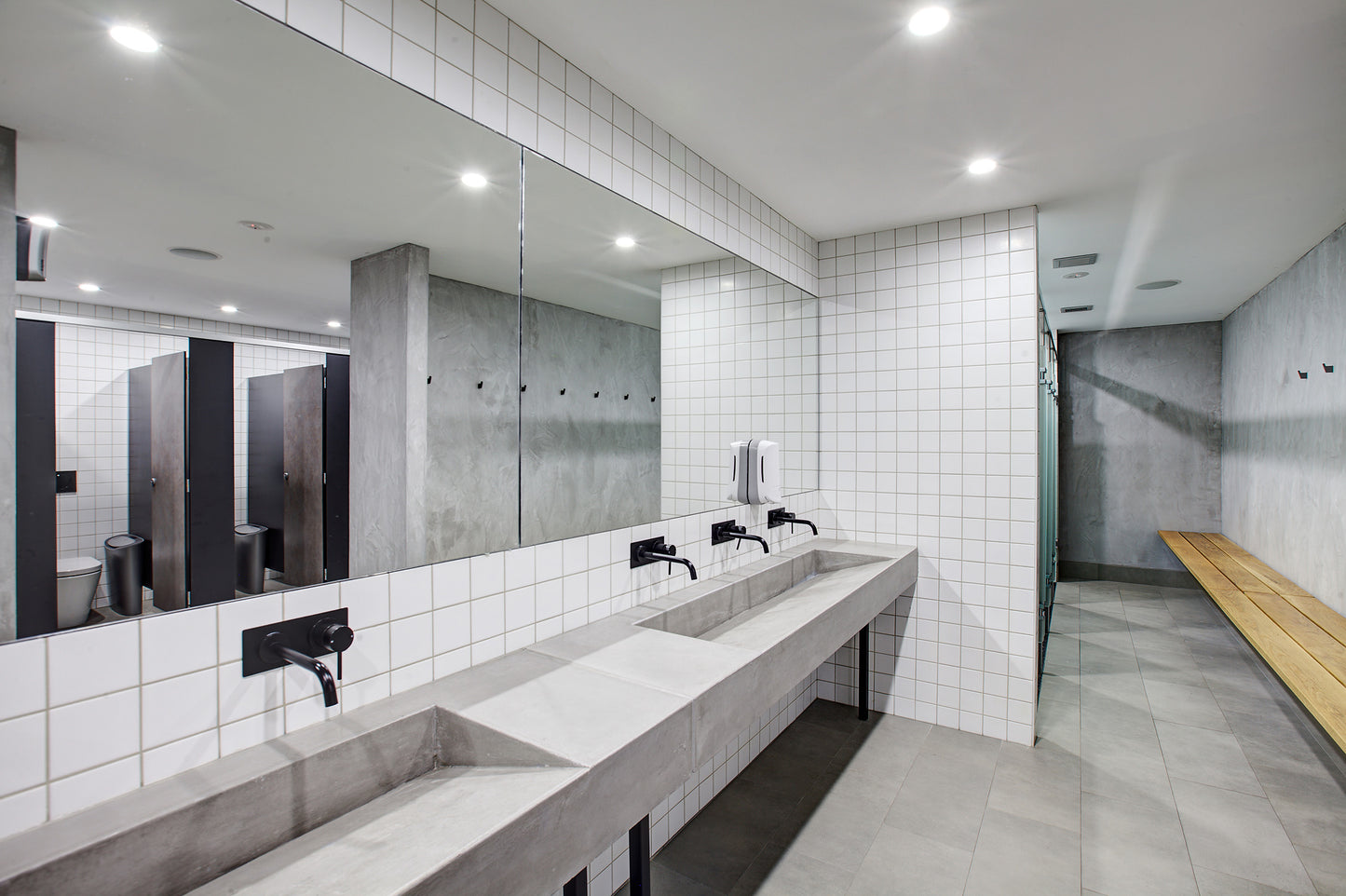 Modern bathroom with concrete sinks tiled walls, and changing room wooden bench.