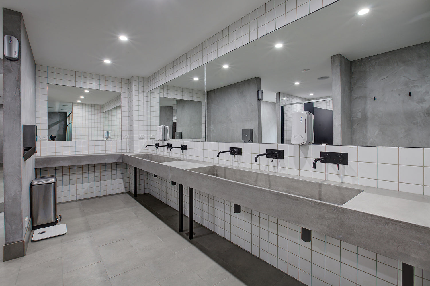 Modern grey bathroom with custom concrete sinks tiled walls and mirrors.