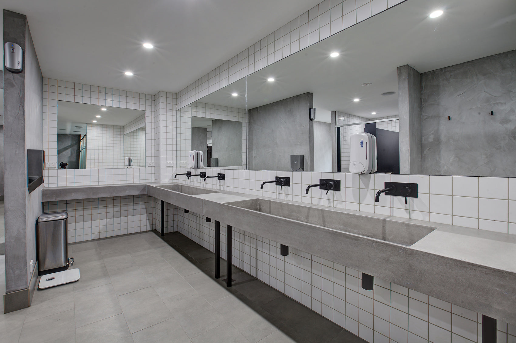Modern grey bathroom with custom concrete sinks tiled walls and mirrors.